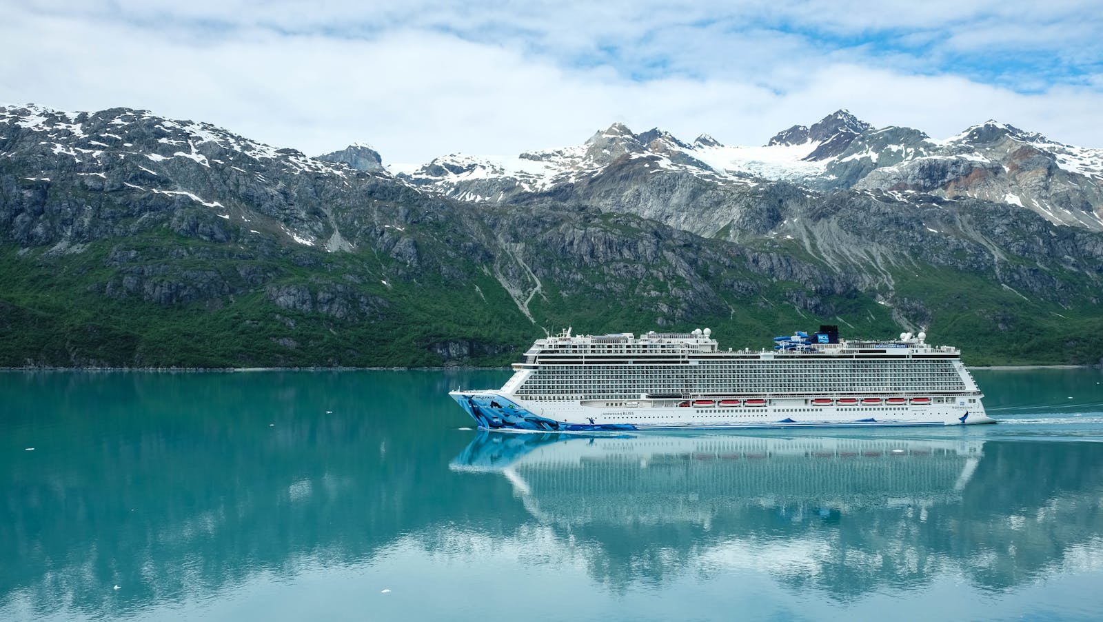 A majestic cruise ship sailing through clear waters with snowy mountains as a backdrop.