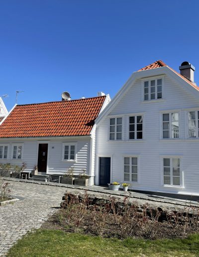 Traditional white wooden houses in Gamle Stavanger, Norway, with red tiled roofs and a cruise ship docked nearby.